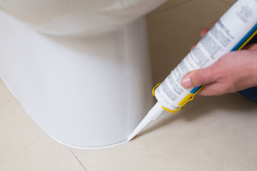 How to use a caulk gun for the first time - man caulking bottom of toilet to floor