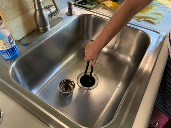 garbage disposal is jammed - woman removing debris from disposer with tongs