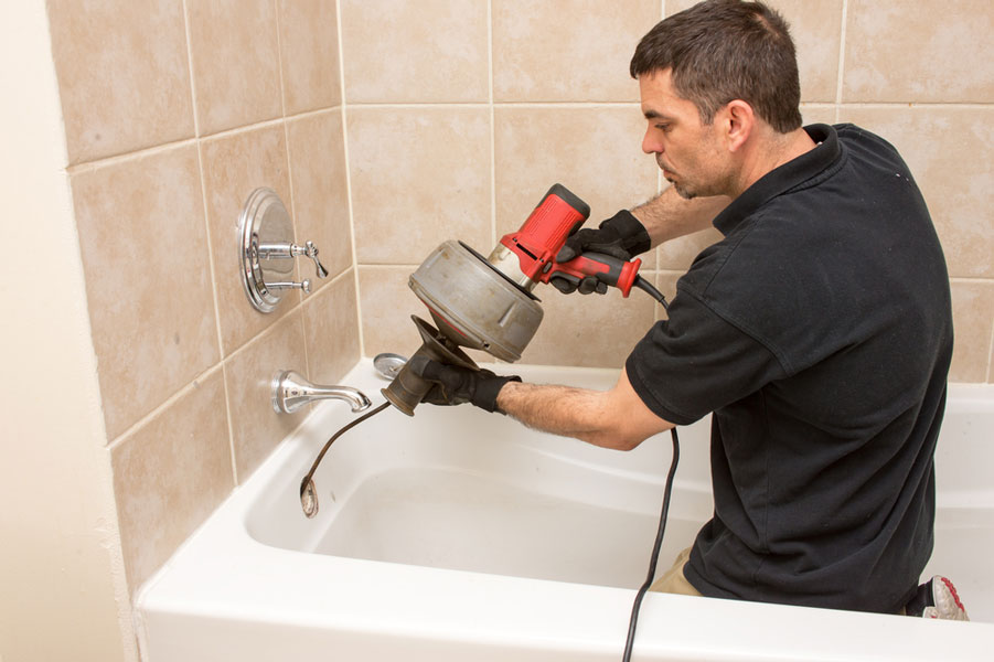 how to use a plumbers snake - man using drain auger on shower drain