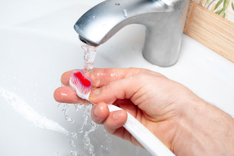 save water in the bathroom - toothbrush being rinsed under bathroom faucet