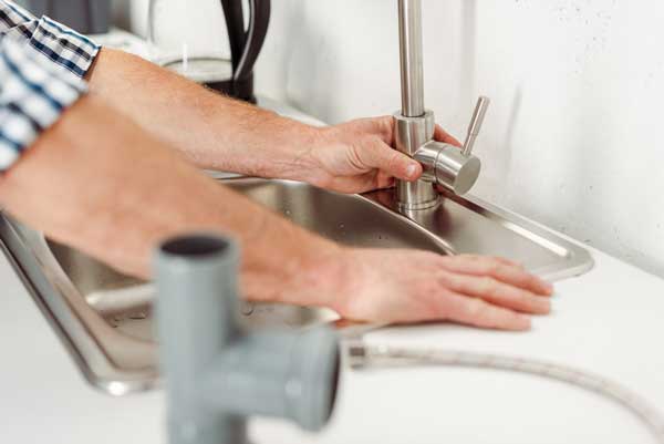 save water in the kitchen - plumber working on faucet to make sure it does not leak