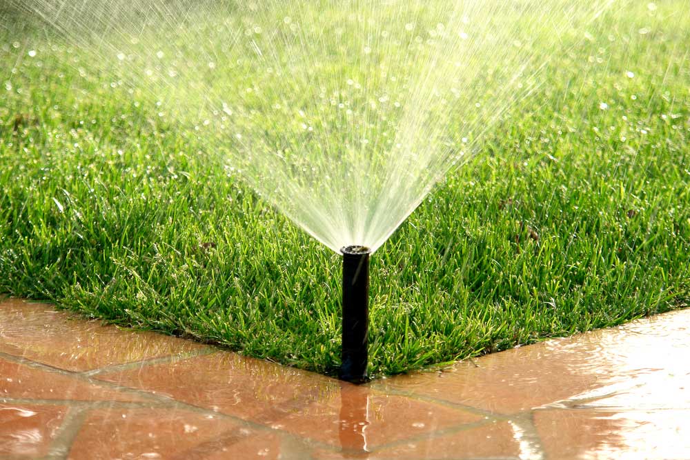 ways to save water outside the home - sprinkler putting water on grass and sidewalk
