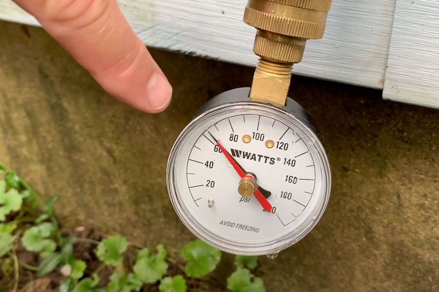 How to test water pressure in home - plumber pointing at water pressure gauge on outdoor faucet