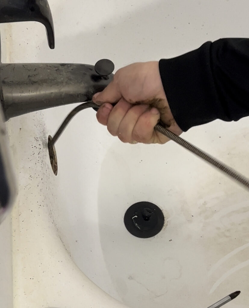 This is a drain auger being used to clear a clogged bathtub drain.